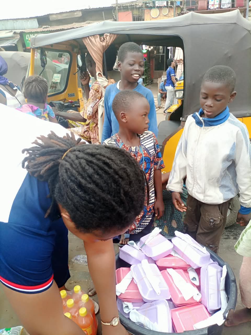 Children gathered around a basin of packed hot meals being served on a Lagos street