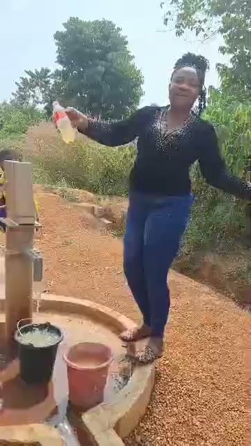 Clean water running from a borehole hand pump provided for a rural community, with Nurse Vivian Okafor celebrating beside it